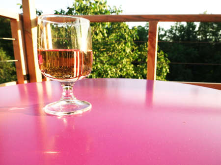 Glass of wine on a pink table with nature in the backgroundの写真素材