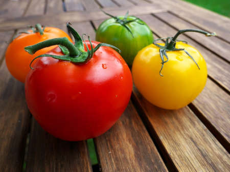 Close-up of green, orange, yellow and red tomatoes on a wooden table. Fresh vegetables of the summer season, to prepare a recipeの写真素材