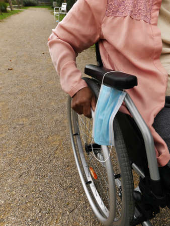 Close-up of the hand of a woman pushing her wheelchair, she put her mask on the armrest.の写真素材