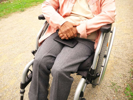 Close-up of the body of an elderly disabled black woman in a wheelchair, holding her phone on her legsの写真素材