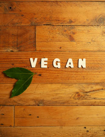 Word "VEGAN" in white letters on a wooden background with two laurel leavesの写真素材