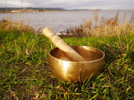 Singing bowl placed on the grass with the pond in the backgroundの写真素材