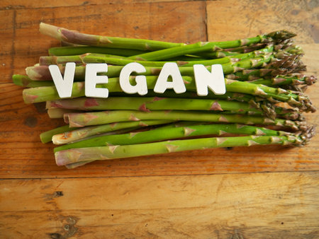 Close-up shot of the letters VEGAN on the wooden brown table and asparagus underneath.の写真素材