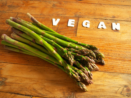 Close-up shot of the letters VEGAN on the wooden brown table and asparagus on the left.の写真素材