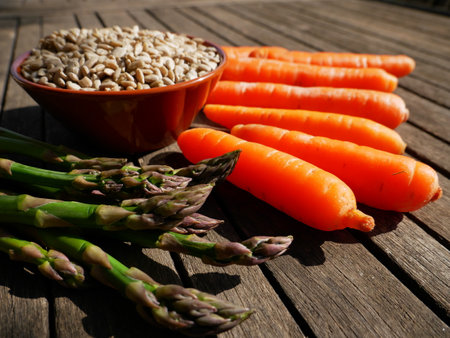Sunflower seeds in a bowl, asparagus and carrots on a wooden table. view from aboveの写真素材