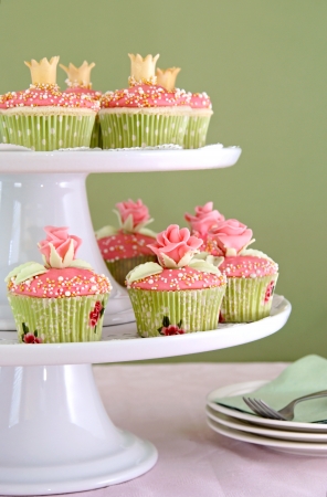 Vanilla cupcakes with pink frosting decorated with roses and crowns made of fondant.                  の写真素材
