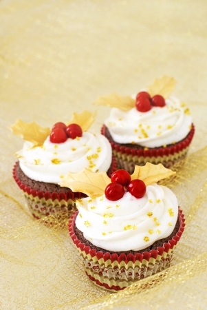 Chocolate cupcakes with vanilla icing and red candy berries and gold fondant leaves               の写真素材