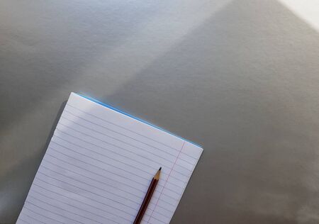 open school notebook with pen on a gray desk with sun rays from the window. A blank, white sheet of notebook for writing. education concept. Copy space. view from above. Flat lay.の写真素材