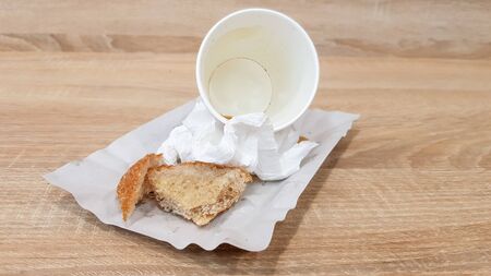 Leftover food on a paper plate and empty dirty paper coffee cup on a wooden table in a fast food...
