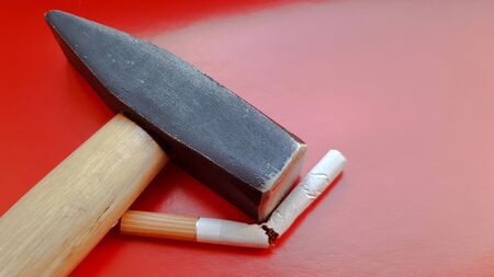Hammer and a broken cigarette on a red background.の写真素材