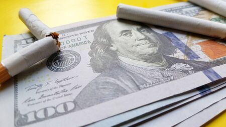 Classic cigarettes stand on one hundred US dollar bills. Cigarettes on a hundred dollar bill on a...