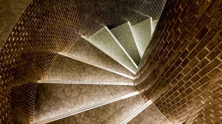 top view of a narrow stone spiral staircase lined with ceramic brown tiles.