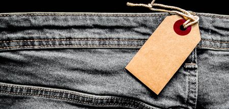 Closeup jeans with blank cardboard white price tag for your text. Tag the white mockup on the blue...
