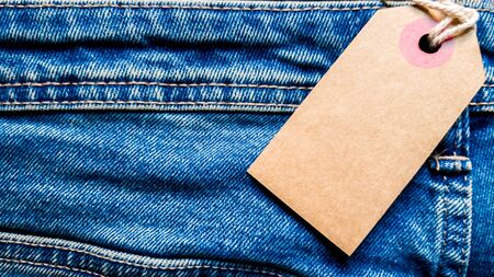 Closeup jeans with blank cardboard white price tag for your text. Tag the white mockup on the blue...