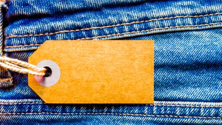Closeup jeans with blank cardboard white price tag for your text. Tag the white mockup on the blue...