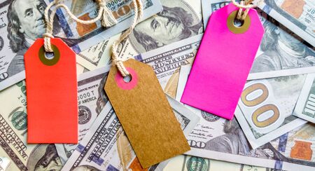 Three empty multi-colored and bright cardboard tags for the inscription Black Friday or discounts on the background of a heap of American hundred-dollar bills.の写真素材