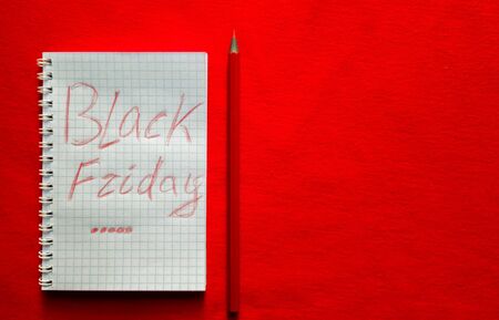 Black friday sale text written on a notepad with a red pencil on a red background. Background,...