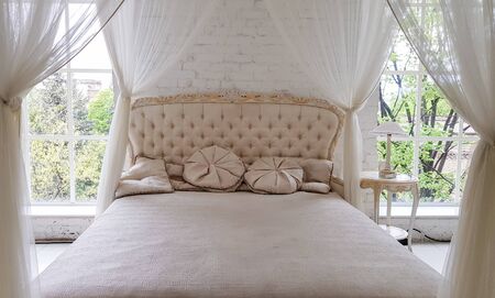 A cozy white wooden bed near a large window with beautiful curtains in the room. Gold-framed modern...