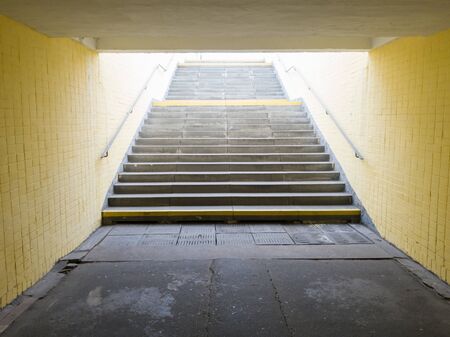 Empty yellow underground pedestrian crossing. Tunnel and daylight at the end. Steps to the top at the pedestrian crossing. A long concrete tunnel with lanterns in the city undergroundの写真素材