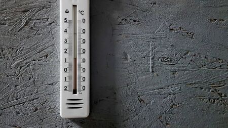 white thermometer hanging on a gray gray wooden wall indoors, background with copy space and empty...