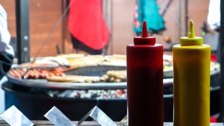 ketchup and mayonnaise in plastic tubes near a street grill in the foreground close-up with selective focus. Barbecue, street food festival. Two cans of meat sauces. Red and yellow containerの写真素材