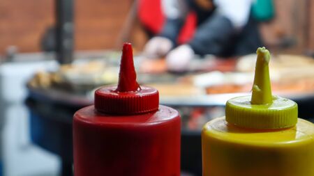 ketchup and mayonnaise in plastic tubes near a street grill in the foreground close-up with...