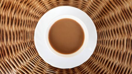 Coffee cup on wicker background top view. Hot aromatic coffee with milk. Freshly prepared drink is served in a modern cup on a light wicker table.の写真素材