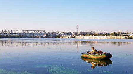 Ukraine, Kiev - August 20, 2019: fishing. Fisherman on an inflatable boat with fishing tackle on a river in the city limits on a sunny summer morningのeditorial素材