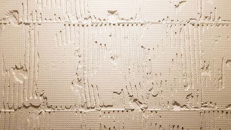 Glue for a tile with a gear pattern. Installation of tiles. The surface of the wall is covered with adhesive paste before laying tiles or decorative stone. Repair work and renovation conceptの写真素材