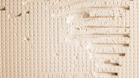 Glue for a tile with a gear pattern. Installation of tiles. The surface of the wall is covered with adhesive paste before laying tiles or decorative stone. Repair work and renovation conceptの写真素材