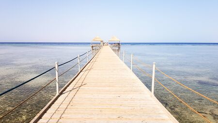 Long pontoon on the Red Sea in Egypt. Pontoon for descent into the water. Wooden bridge on the territory of the Amway Hotel in Sharm El Sheikh with metal fences and a rope over the sea with waves.の写真素材