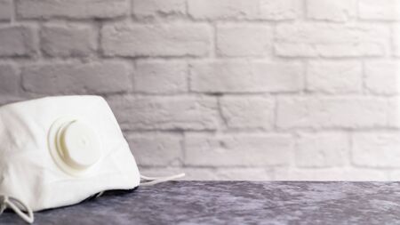 White face shield with flap on a gray table against a white brick wall with copy space. medical masks during outbreaks of viral diseases such as coronavirus or COVID-19 pandemicの写真素材