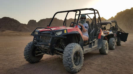 Egypt, Sharm El Sheikh - October 10, 2020. Active woman driving an ATV on a dirt road in the desert against the backdrop of rocky sandy mountains in the sunsetのeditorial素材