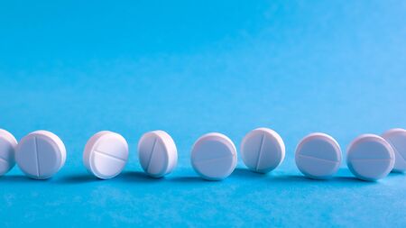 White round medical pills on a blue background. Scattered white pills on the table. The concept of medicine, pharmacy and healthcare. Copy space Empty space for text or logoの写真素材