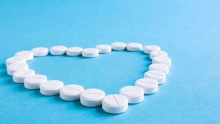 White round pills laid out in the shape of a heart on a blue background. Health symbol made of pills...