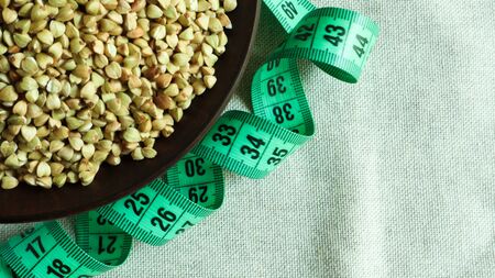 Green measuring tape on a background of raw buckwheat in a dish, concept of diet and healthy...