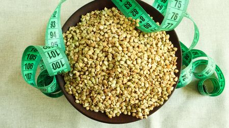 Green measuring tape on a background of raw buckwheat in a dish, concept of diet and healthy...