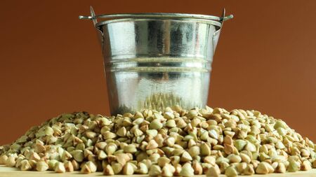 Small metal bucket with raw buckwheat on a board on a brown background. Organic vegetarian food. The concept of a healthy and balanced diet. Dietary nutrition. Copy space.の写真素材