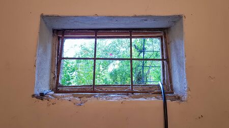 A rectangular basement window is tightened with a metal mesh and a grill. Technical window in the...