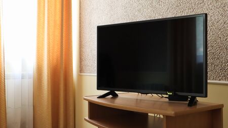 Hand holding a television remote control and surfing programs on television. watch, turn on or off the TV in the living room or bedroom on the black-screen nightstand. Copy spaceの写真素材