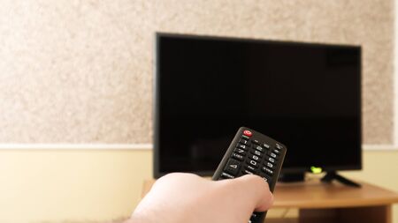 Hand holding a television remote control and surfing programs on television. watch, turn on or off the TV in the living room or bedroom on the black-screen nightstand. Copy spaceの写真素材