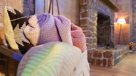 Knitted and warm blankets are folded and laid in a wicker basket near the fireplace. Cozy interior in the house. Details of a modern cozy interior.の写真素材