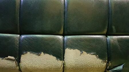 Torn and battered leather of a green sofa. Poor quality leather, cleaning and restoration of the skin. Detail of an old vintage leather armchairの写真素材
