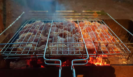 The process of cooking shish kebab on the grill. Juicy and fragrant meat languishes on fire and smoke. Countryside picnic concept at night. Appetizing and nutritious picnic dish in the open airの写真素材