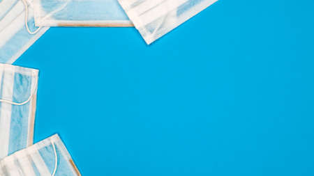 Many antiviral protective medical face masks with earloops are set against a blue background....