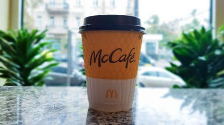 McDonald's logo on a yellow paper cup with hot McCafe coffee near the window. Fast food chain....