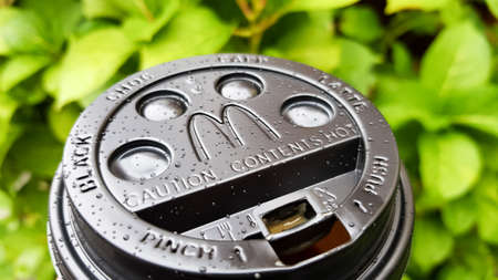 Close-up of McDonald's fast food restaurant logo on a black paper cup lid with hot McCafe coffee....