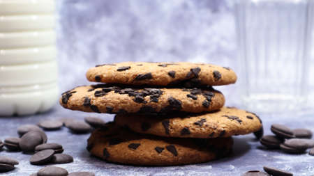 American chocolate chip cookies stacked on top of each other with milk in a glass on a gray...