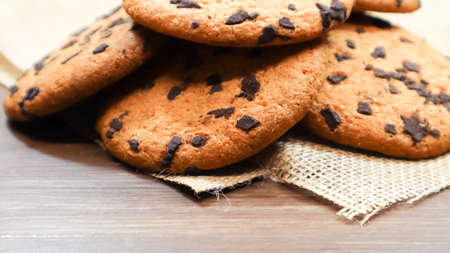 American chocolate chip cookies on a brown wooden table and on a linen napkin close-up. Traditional rounded crunchy dough with chocolate chips. Bakery. Delicious dessert, pastries. Rural still lifeの写真素材