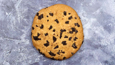 One soft, freshly baked chocolate chip cookie on a gray marble kitchen countertop. American...